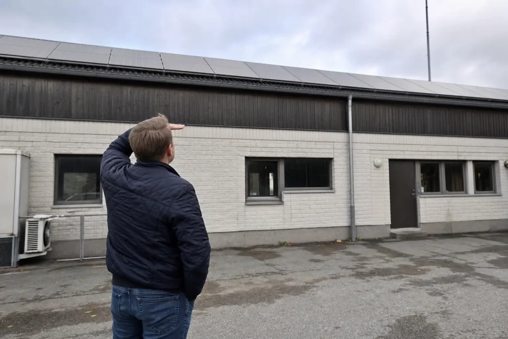 Företagare utanför sitt industribyggnad i Sverige blickar upp mot solpanelerna på taket i dagsljus.